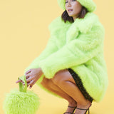 Person wearing a bright green fur like coat with matching hat and purse on a yellow background