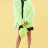 Person wearing a bright green fur like coat with matching hat and purse on a yellow background
