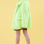 Person wearing a bright green fur like coat on a yellow background