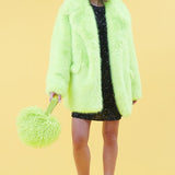 Person wearing a bright green fur like coat with matching purse on a yellow background