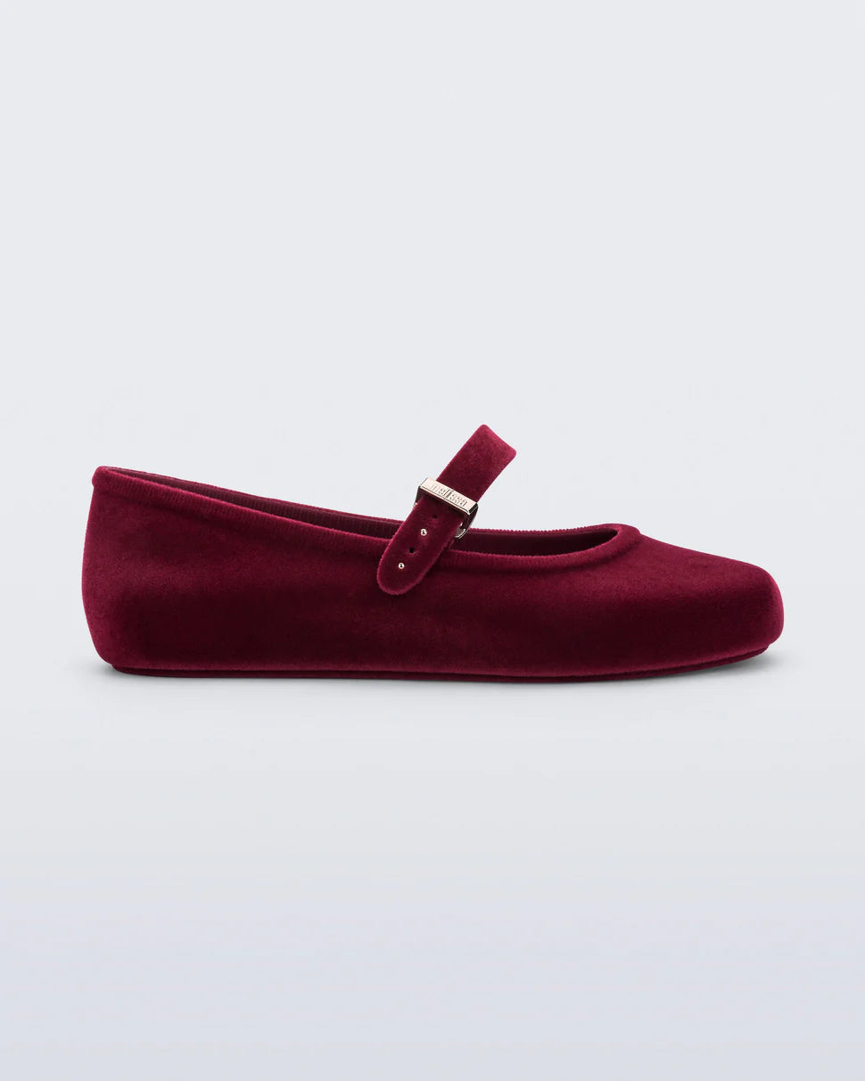 Melissa Soft Ballerina Velvet flat in red. Classic women's ballet flat features flocked finish, mimicking velvet, a fun bubblegum scent, adjustable buckle strap, and rounded toe side profile