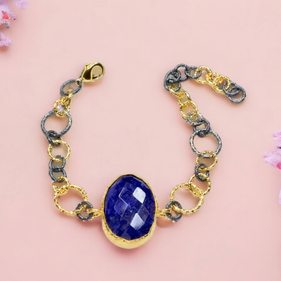 Gold and silver colored large loop chain  bracelet with blue stone on a light pink background