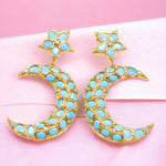 Gold and turquoise colored moon and star shaped earrings on a pink fabric background