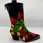 A black mid-calf boot featuring vibrant, colorful floral embroidery in red, pink, yellow, and green, with a black leather pull tab and a low black block heel.