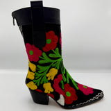 A black mid-calf boot featuring vibrant, colorful floral embroidery in red, pink, yellow, and green, with a black leather pull tab and a low black block heel.