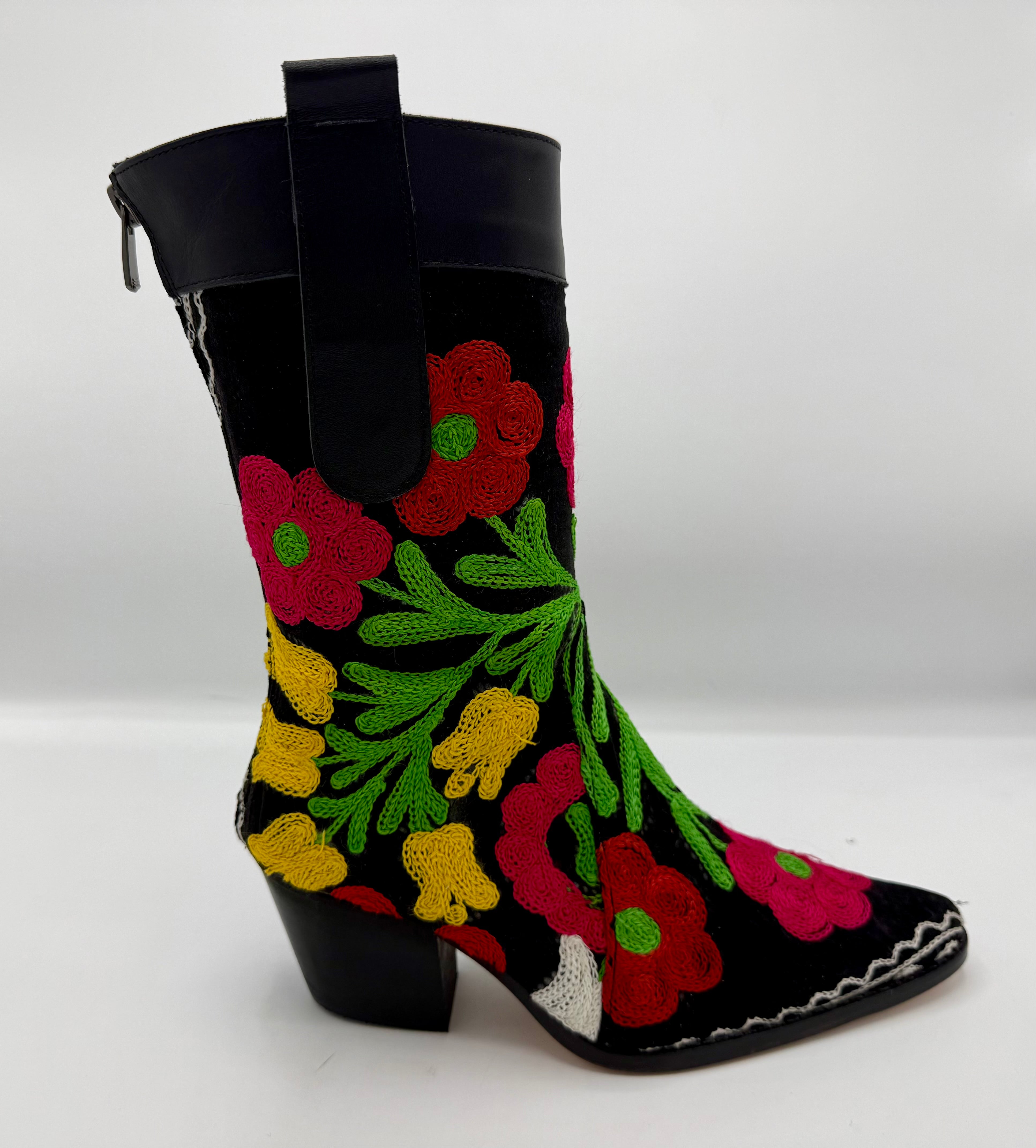 A black mid-calf boot featuring vibrant, colorful floral embroidery in red, pink, yellow, and green, with a black leather pull tab and a low black block heel.