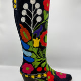 A black suede cowboy boot with vibrant multicolor floral embroidery, featuring a low black block heel