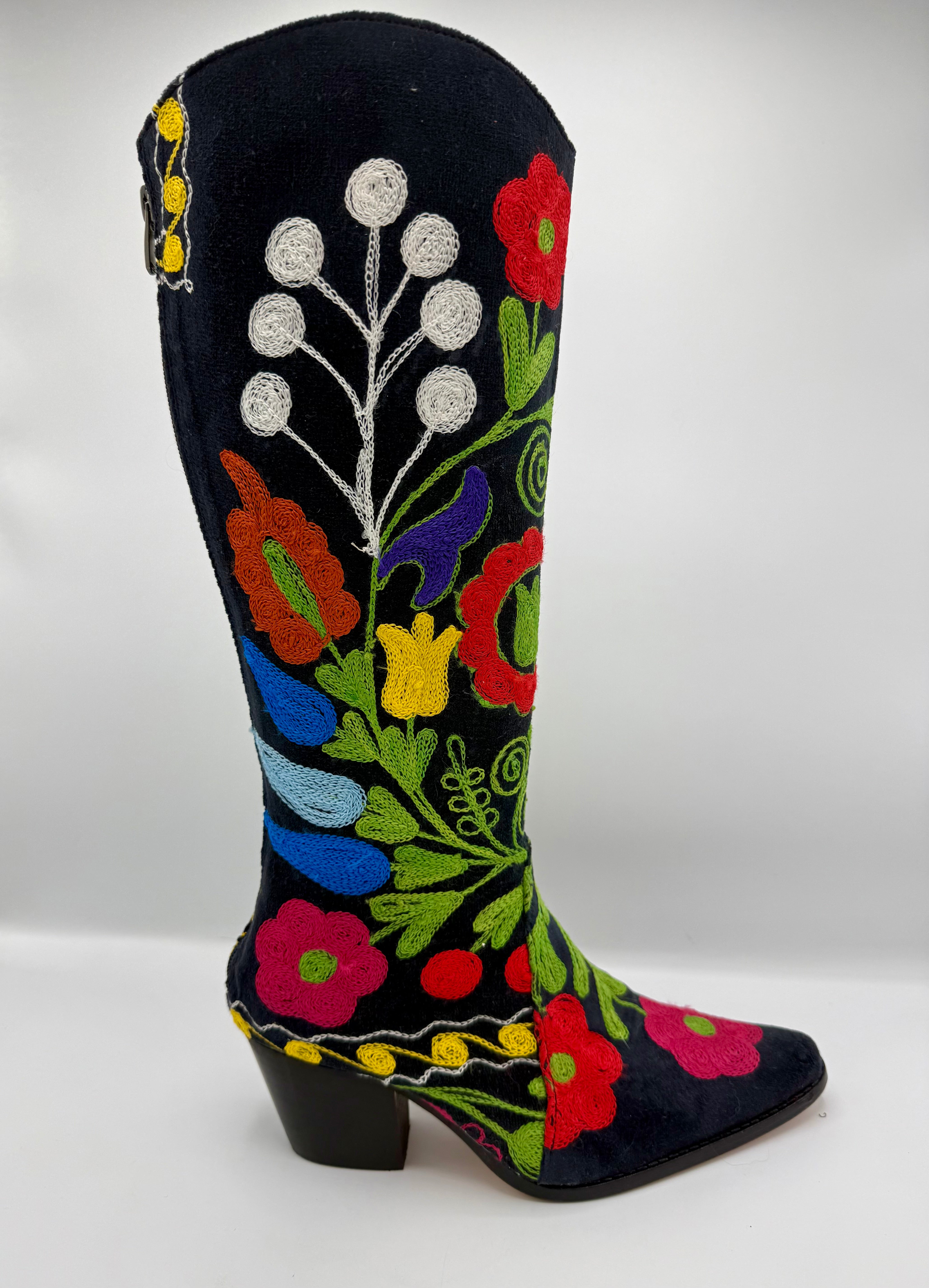 A black suede cowboy boot with vibrant multicolor floral embroidery, featuring a low black block heel