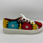 A low-top canvas sneaker featuring vibrant, multicolor floral embroidery in red, blue, yellow, and green on a black background, with white laces and a white rubber sole.