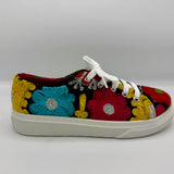 A low-top canvas sneaker featuring vibrant, multicolor floral embroidery in red, blue, yellow, and green on a black background, with white laces and a white rubber sole.