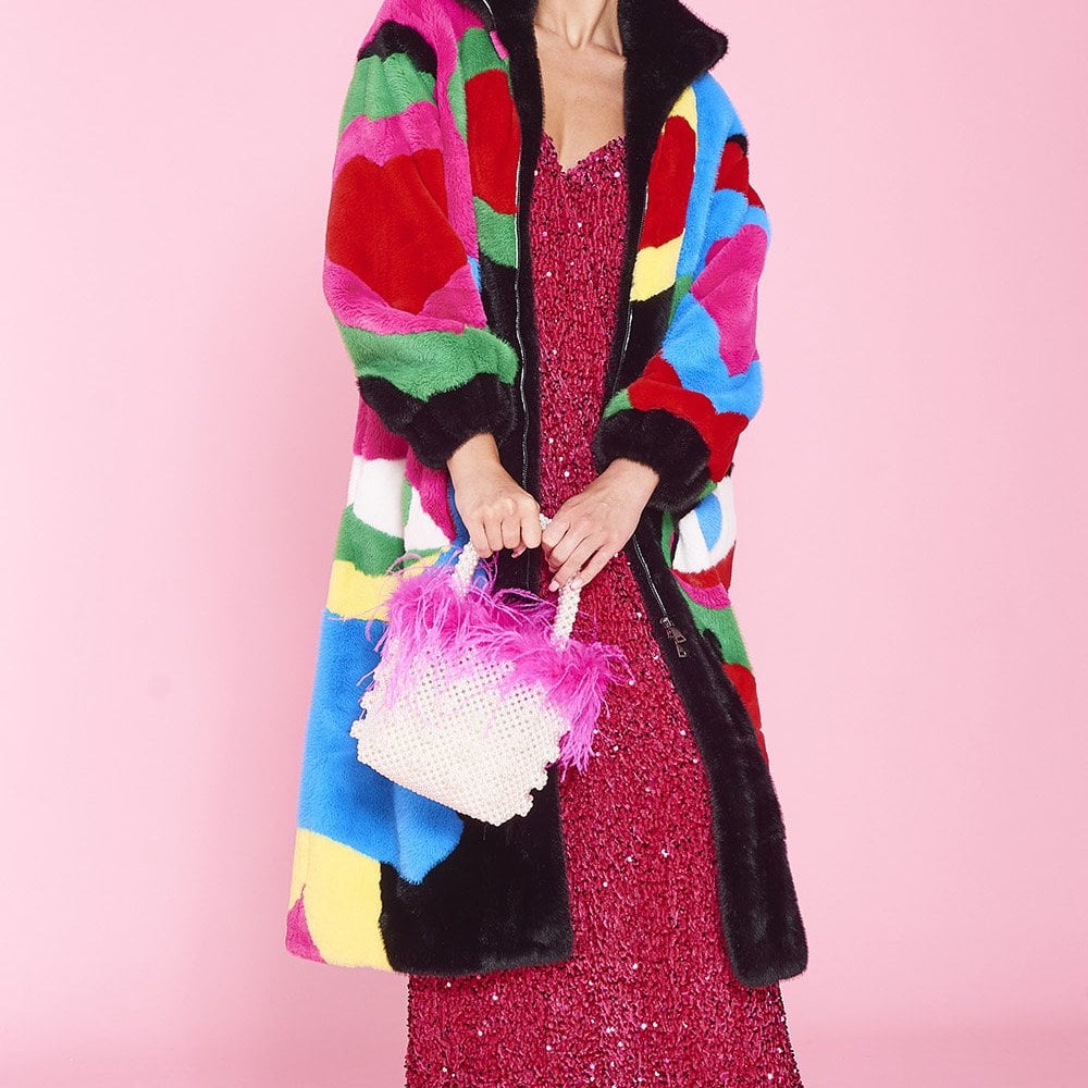 Person wearing a colorful fur like long length coat with heart and face patterns on a pink background