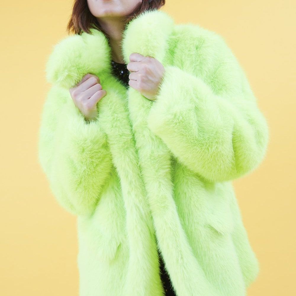 Person wearing a bright green fur like coat on a yellow background