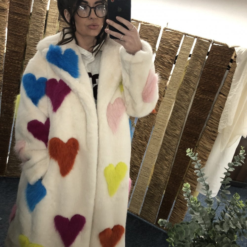 Person wearing a white coat with colorful heart patterns, taking a mirror selfie.
