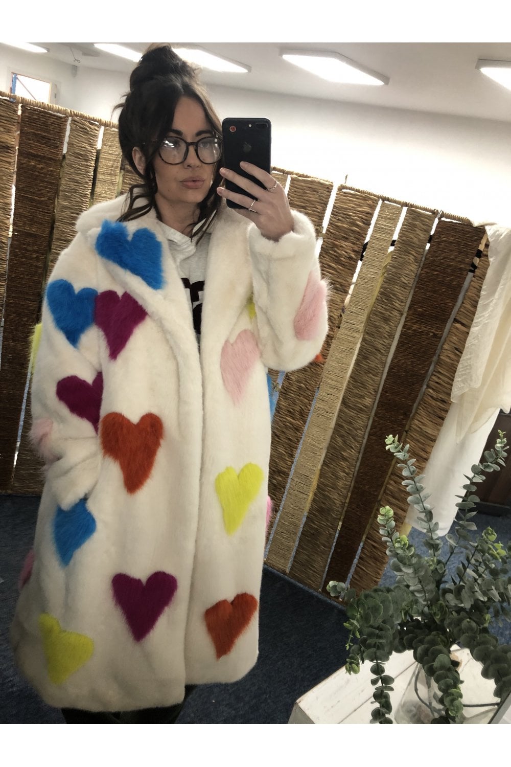 Person wearing a white coat with colorful heart patterns, taking a mirror selfie.