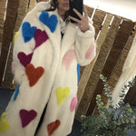 Person wearing a white coat with colorful heart patterns taking a mirror selfie.
