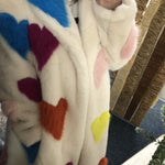 Person wearing a white coat with colorful heart patterns, sitting on a wooden bench.
