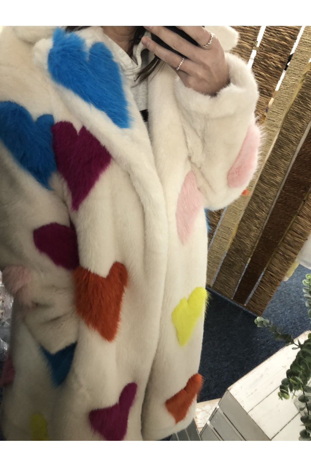 Person wearing a white coat with colorful heart patterns, sitting on a wooden bench.