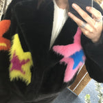 Person wearing a black coat with colorful fur star shaped patches, taking a mirror selfie.