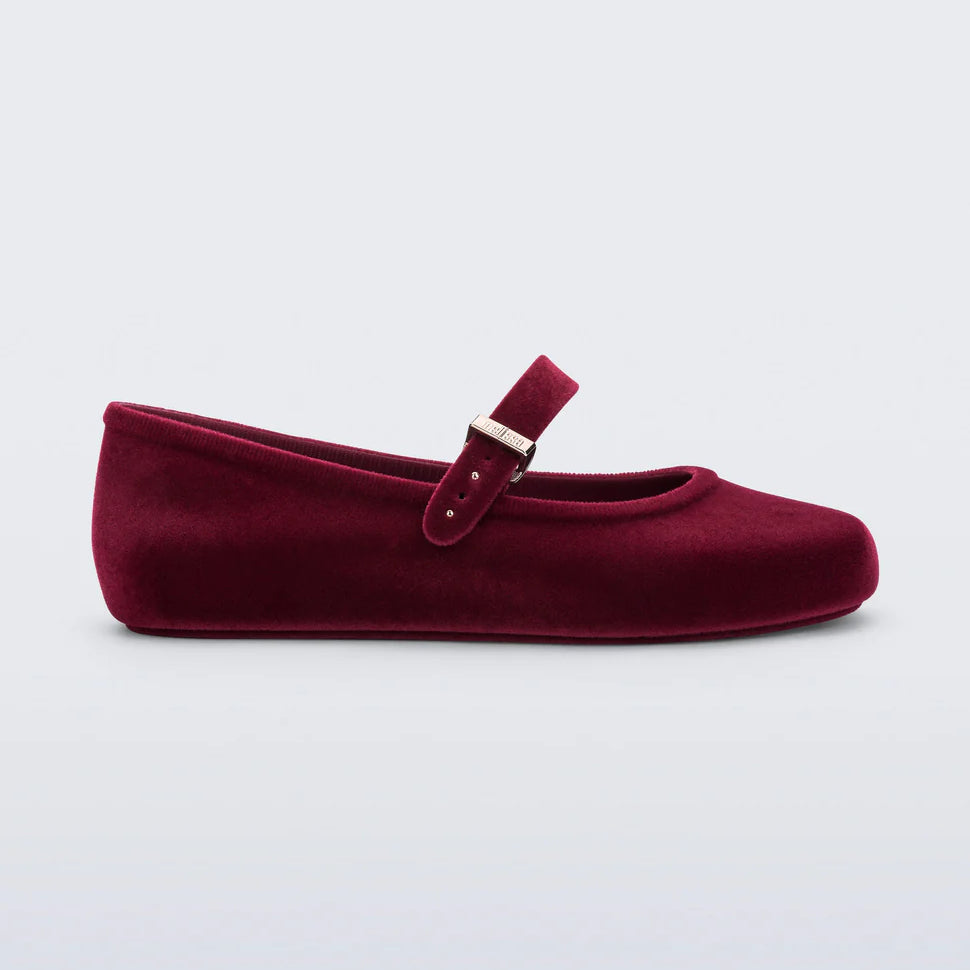 Melissa Soft Ballerina Velvet flat in red. Classic women's ballet flat features flocked finish, mimicking velvet, a fun bubblegum scent, adjustable buckle strap, and rounded toe side profile