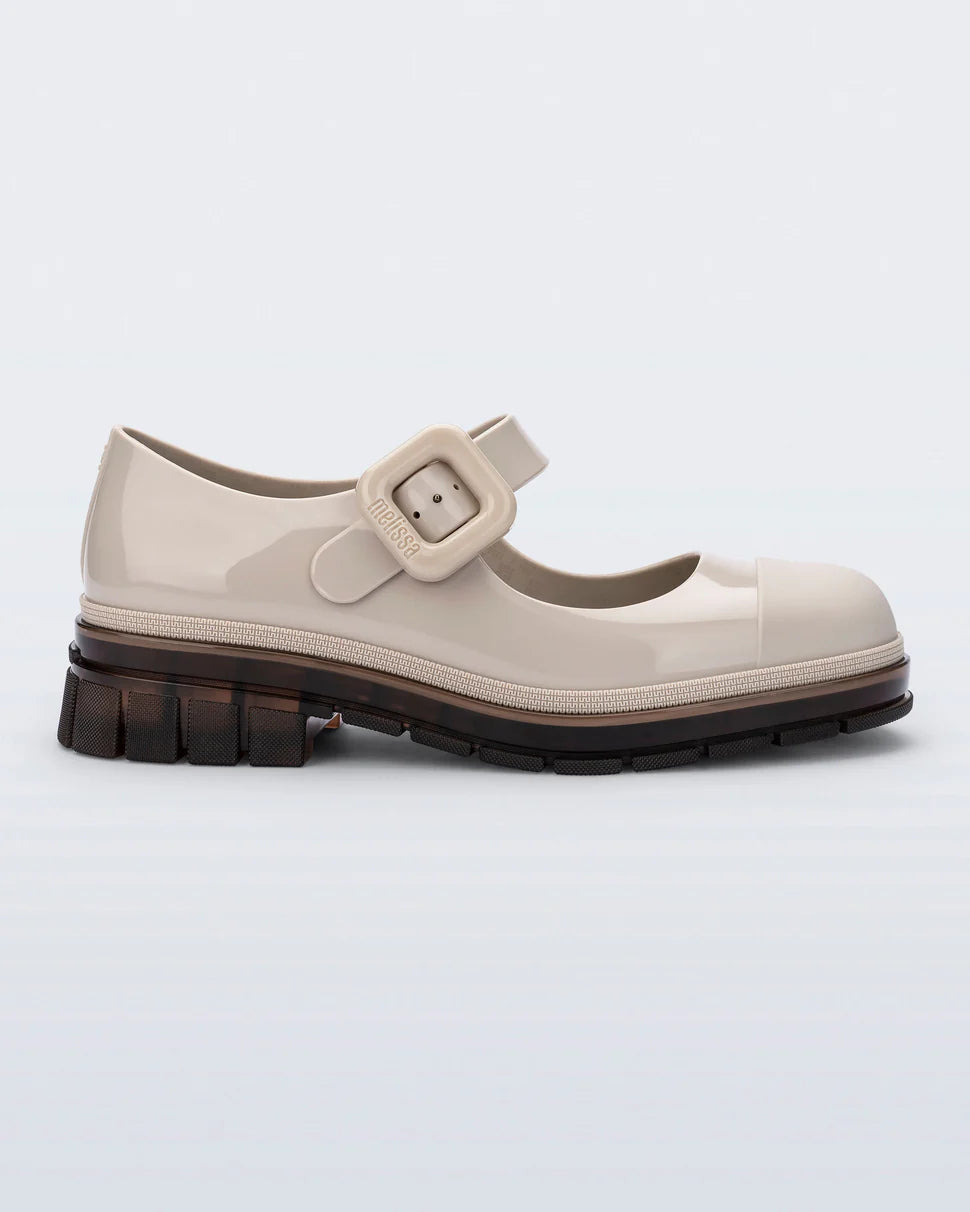 The June  Mary Jane by Melissa features a neutral beige hue, slight heel, fun bubblegum scent, and large buckle detail side profile