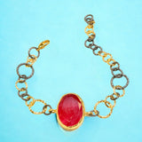 Bracelet with a red stone center on a gold and silver large loop chain on a blue background