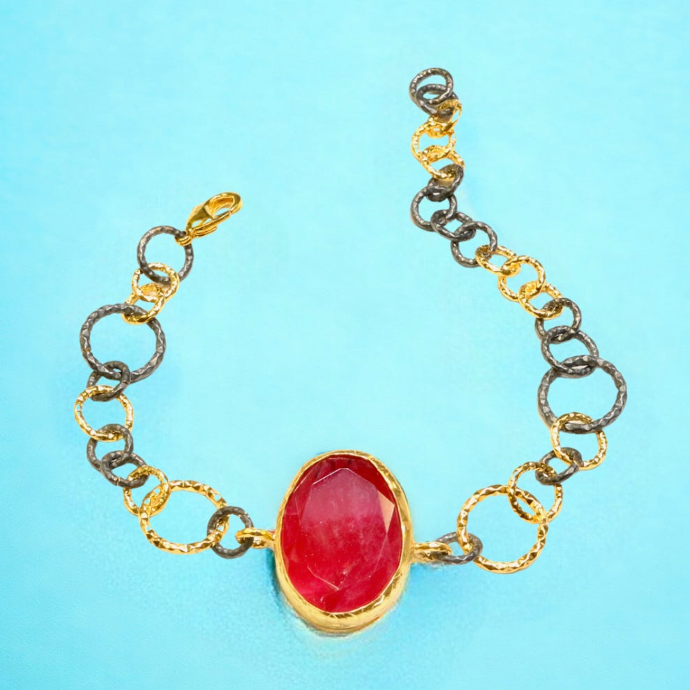 Bracelet with a red stone center on a gold and silver large loop chain on a blue background