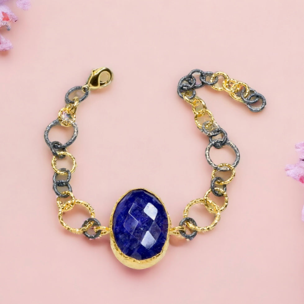 Gold and silver colored large loop chain  bracelet with blue stone on a light pink background