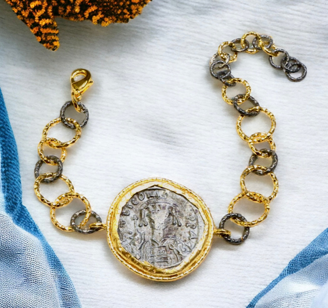 Bracelet with gold and silver large loop chain and coin charm on a fabric background
