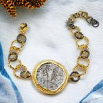 Bracelet with gold and silver large loop chain and coin charm on a fabric background