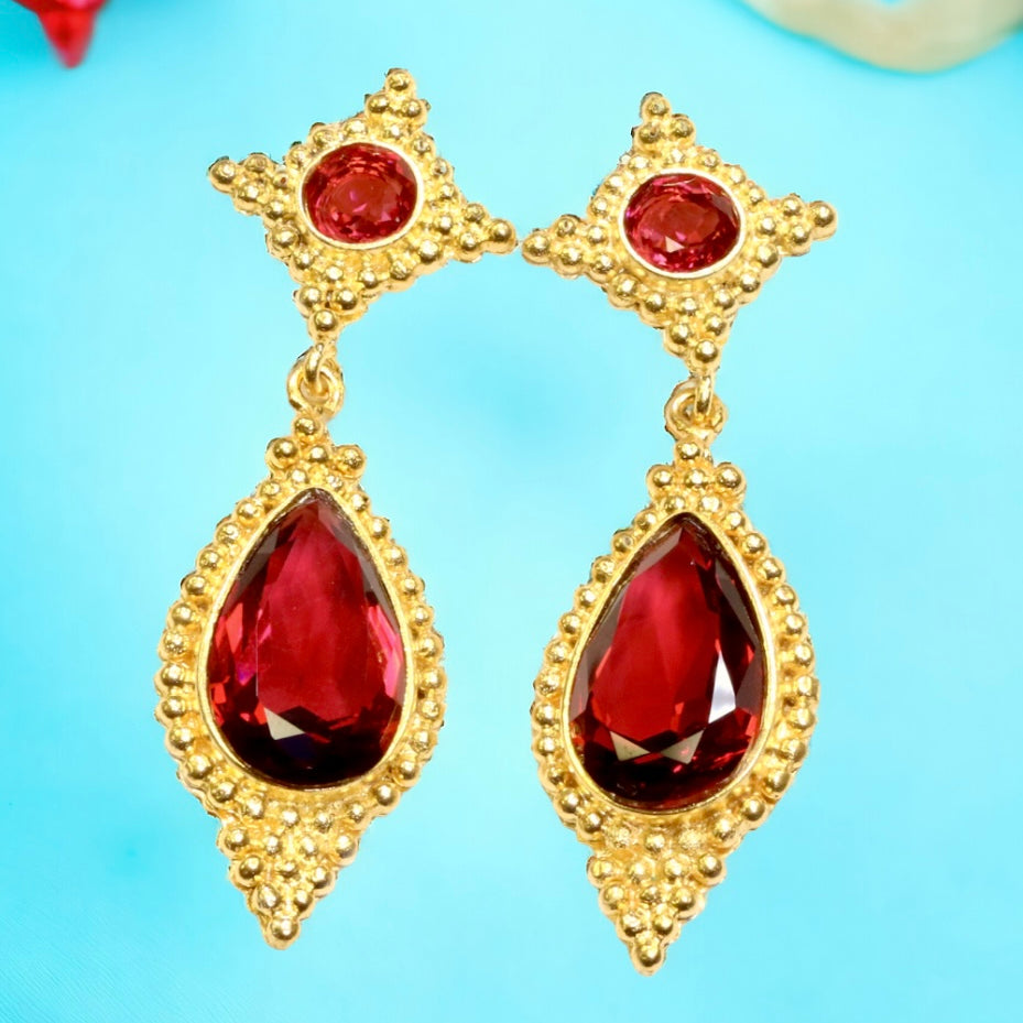 Gold earrings with red gemstones on a light blue background