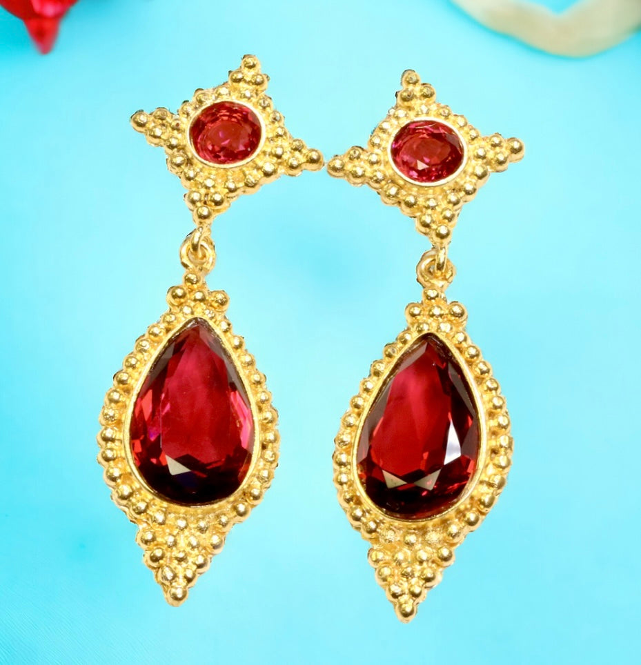 Gold earrings with red gemstones on a light blue background