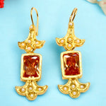 Gold colored earrings with orange stones and pearl like beads on a light blue background