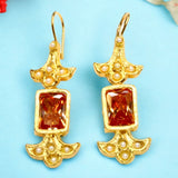 Gold colored earrings with orange stones and pearl like beads on a light blue background