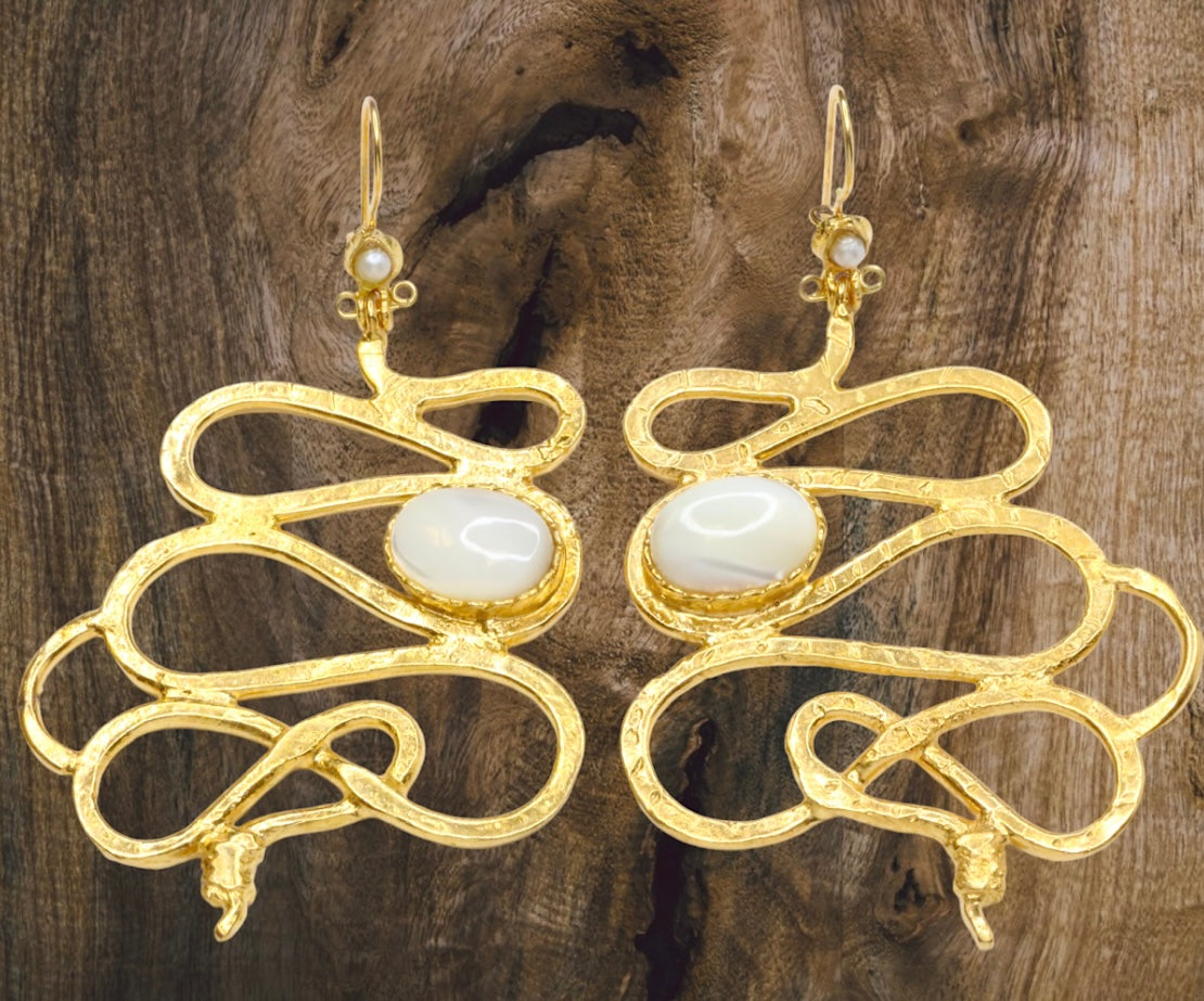 Gold colored snake shaped earrings with white stone accents on a brown wood background
