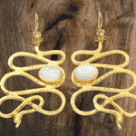 Gold colored snake shaped earrings with white stone accents on a brown wood background