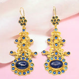 Gold colored earrings with blue stone accents on a pink fabric background