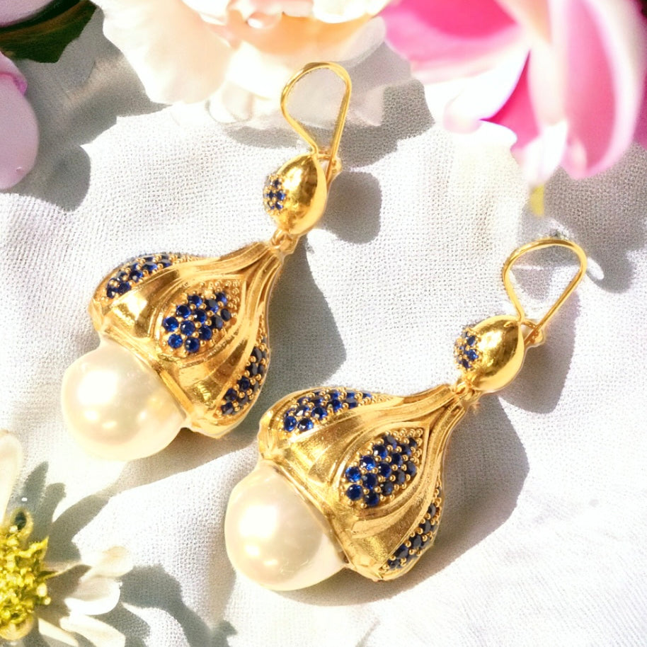 Gold colored earrings with pearl like accent and blue crystals on a white fabric background with flowers