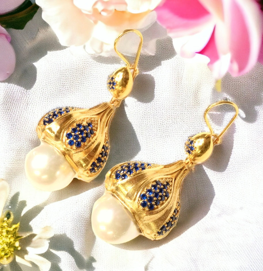 Gold colored earrings with pearl like accent and blue crystals on a white fabric background with flowers