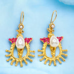 Gold colored earrings with pearl like beading and pink crystal accents on a light blue background