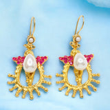 Gold colored earrings with pearl like beading and pink crystal accents on a light blue background