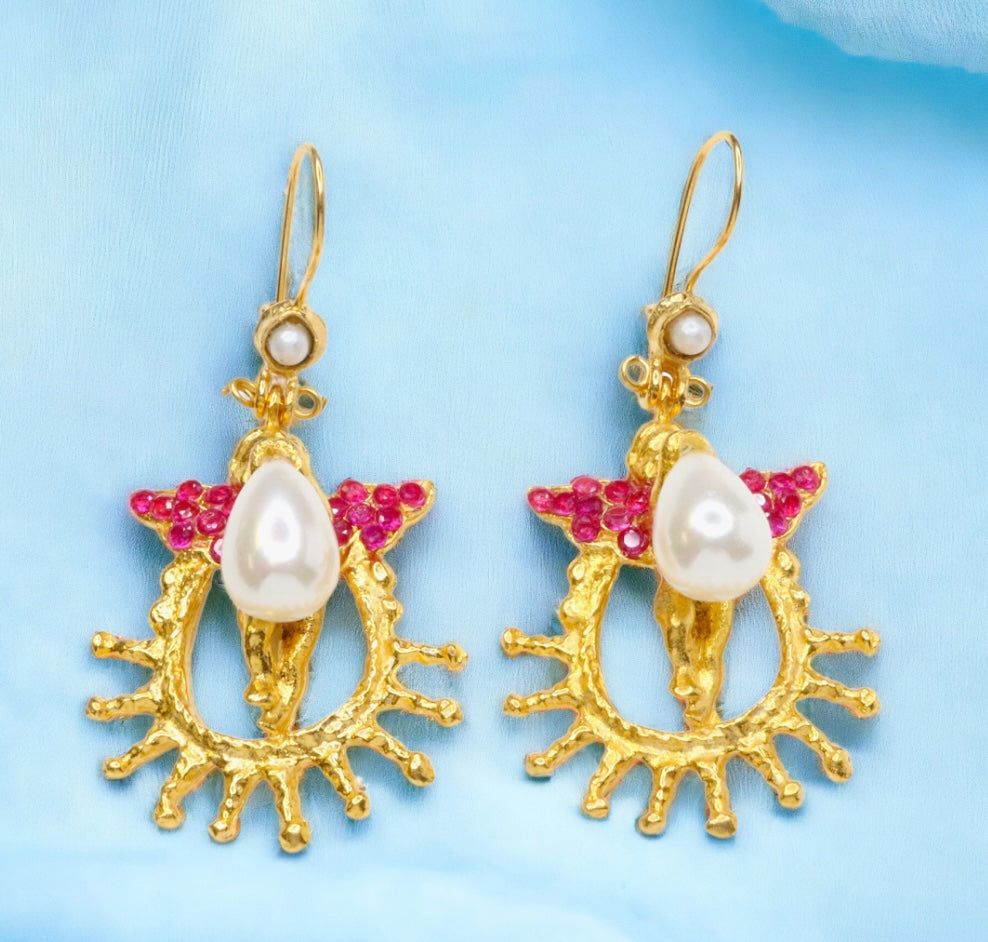 Gold colored earrings with pearl like beading and pink crystal accents on a light blue background
