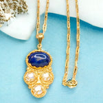 Gold colored necklace with a blue pendant and pearl-like elements with elongated link chain