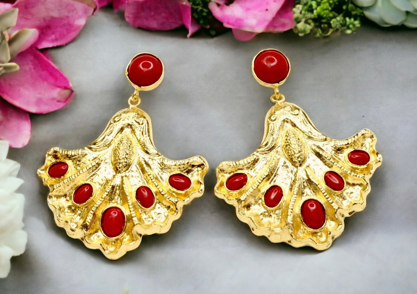 Gold colored earrings with red stone accents on a gray background with flowers