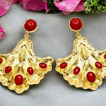 Gold colored earrings with red stone accents on a gray background with flowers