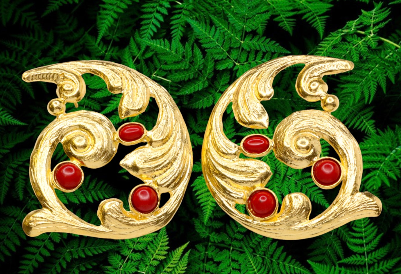 Pair of gold colored earrings with red stones accents on a green leaf background