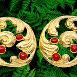 Pair of gold colored earrings with red stones accents on a green leaf background