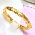 Gold bangle bracelet with a white bead on a pink and white background