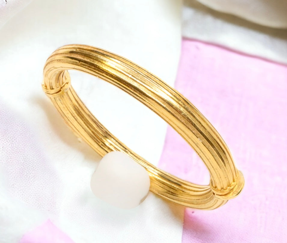 Gold bangle bracelet with a white bead on a pink and white background