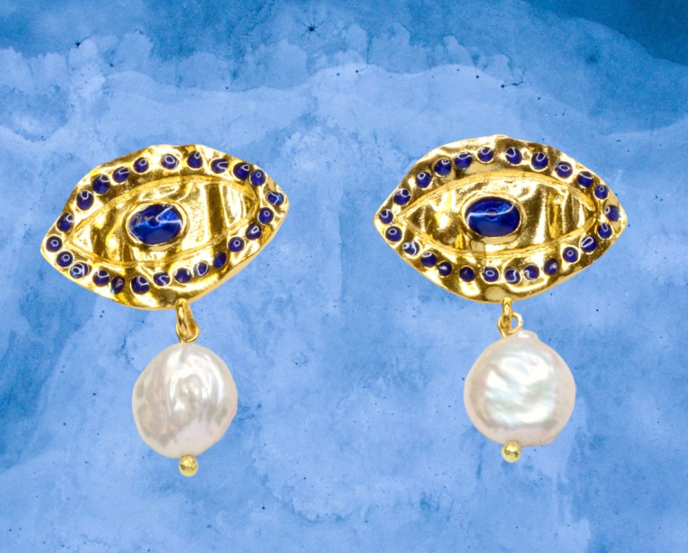Gold colored eye shaped earrings with blue stones and pearl like accent drops on a blue background