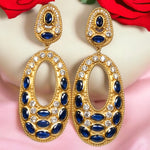 Gold colored earrings with dark blue and white crystal accents on a pink and white background